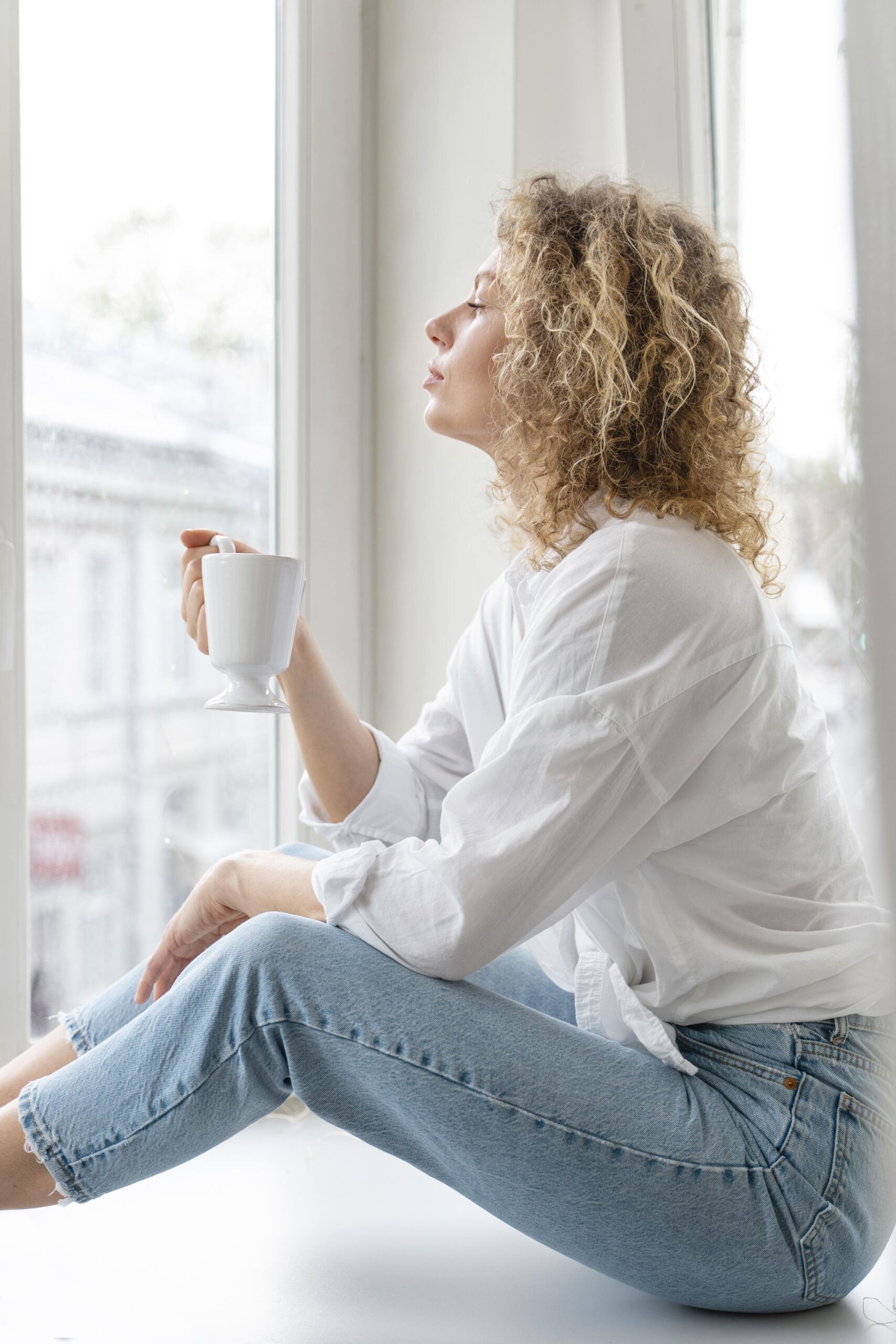 Side view curly haired blonde woman relaxing home with coffee cup